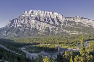 A forest and river in the foreground. In the background a mountain range looms large.