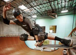 Tony Hawk grabs his skateboard while flying above an indoor vert ramp.